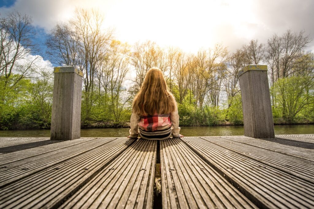 femme assise de dos au bord d'un quai lors d'une journée ensoleillée